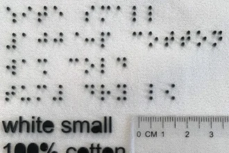 Izabela Ciesielska-Wrobel, assistant professor of textiles, fashion merchandising and design in URI’s College of Business, showing the size of the braille symbols compared to regular washing instructions. (URI photo/Izabela Ciesielska-Wrobel)