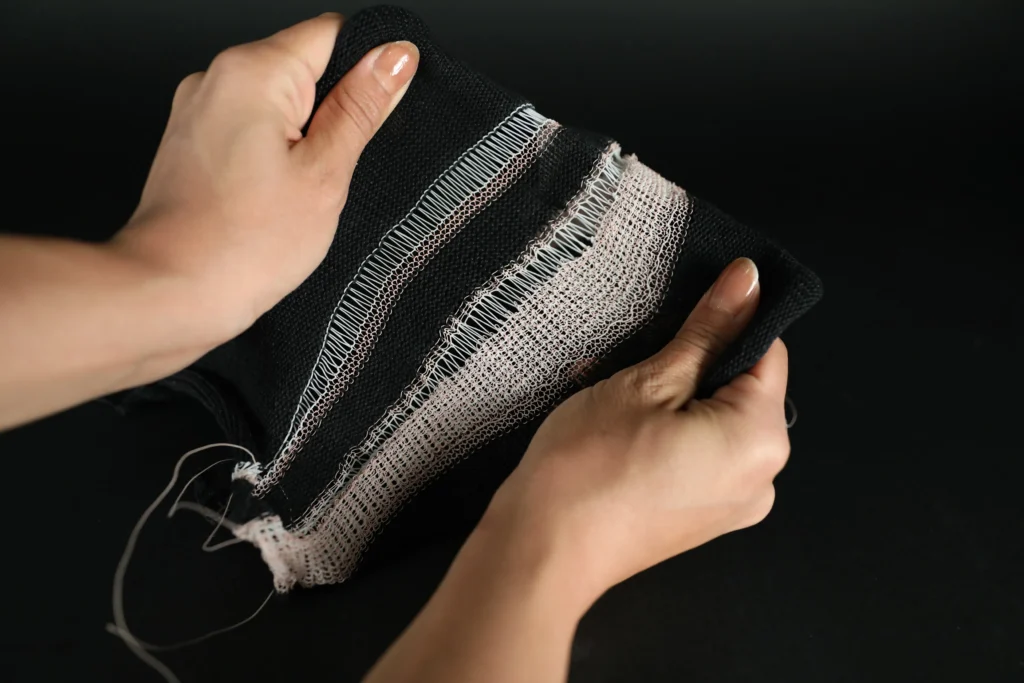 Hands stretching a black knit sample embedded with LCE FibeRobo fibres