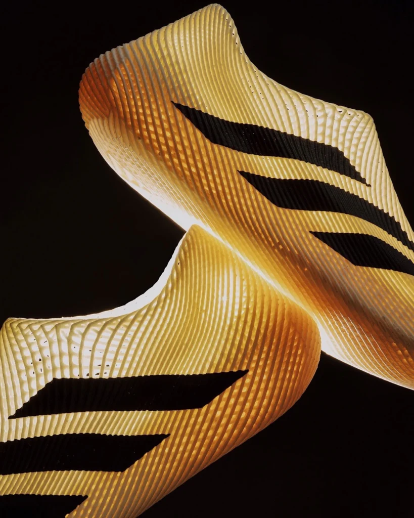Close‑up macro of the golden polyurethane lattice with ghosted Three‑Stripes on the new Climacool 3D‑printed slip‑on.