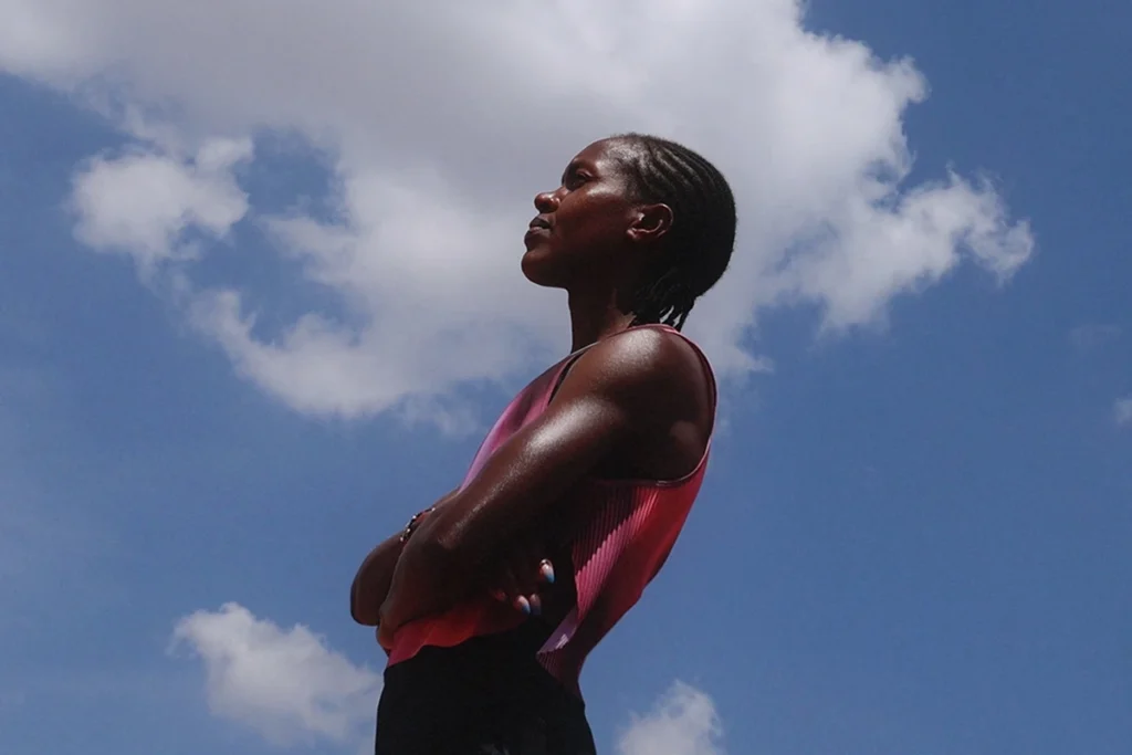 Portrait of Faith Kipyegon wearing magenta FlyWeb test top, arms folded against clear sky.