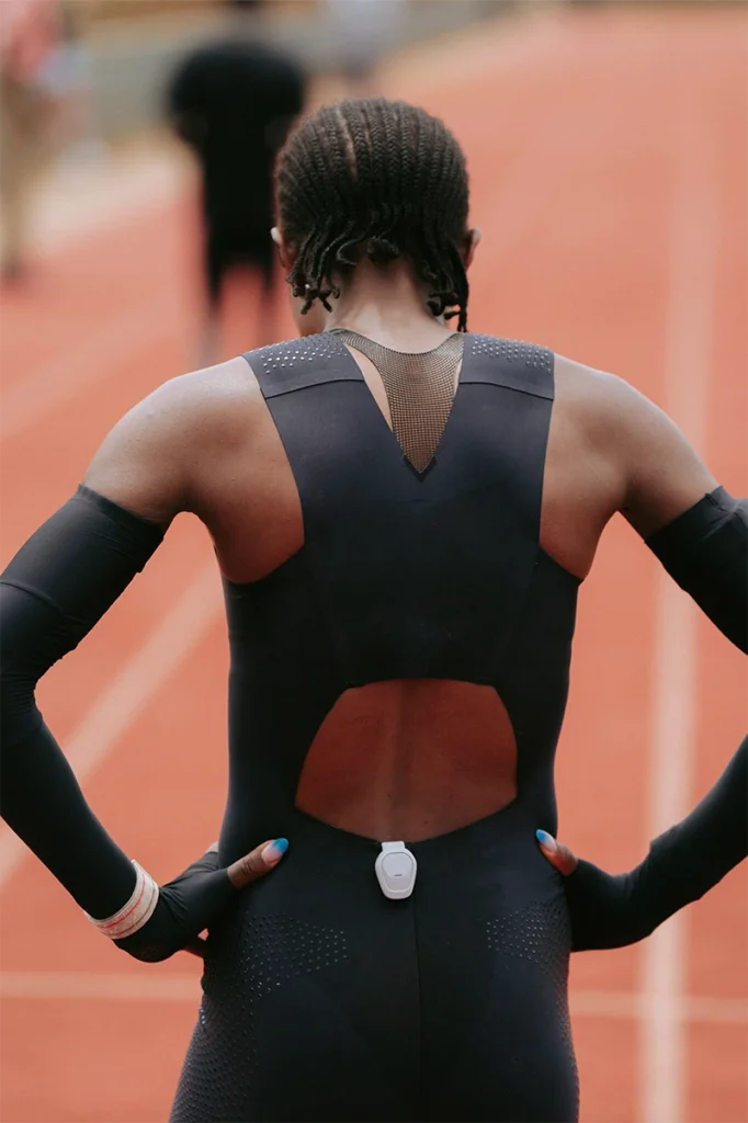 Rear view of Faith Kipyegon running in Breaking4 speedsuit with FlyWeb bra visible through back cut-out on training track.