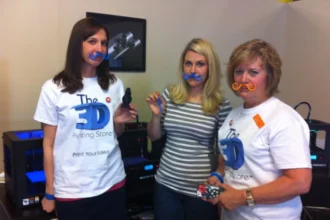 Team at The 3‑D Printing Store in Denver posing with colorful 3‑D‑printed mustaches and mini objects.