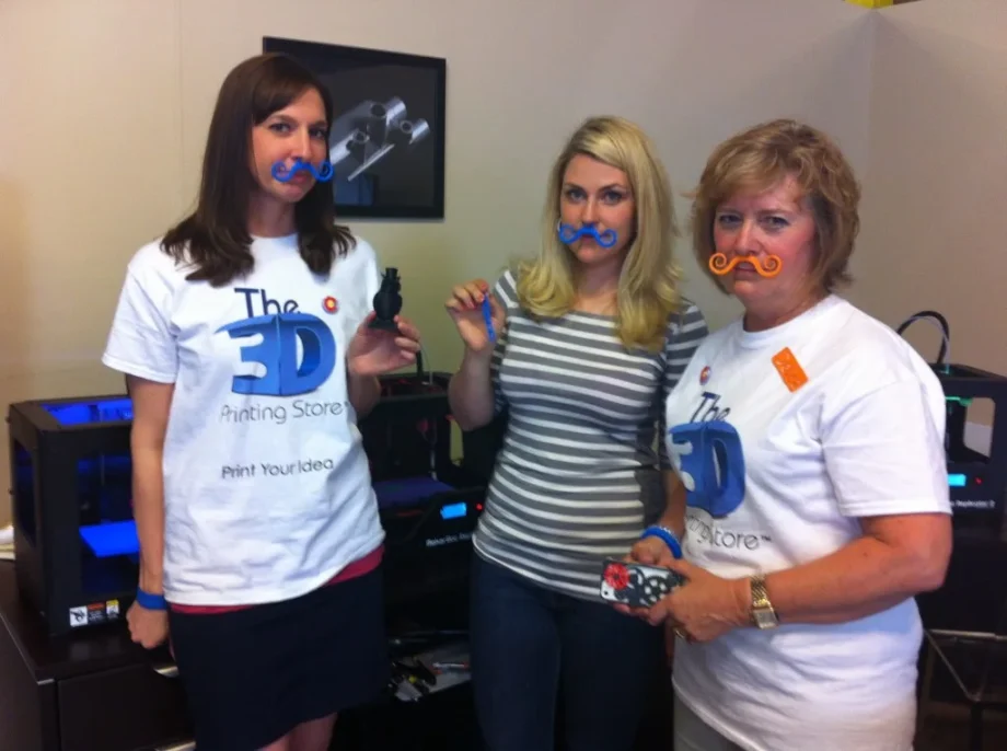 Team at The 3‑D Printing Store in Denver posing with colorful 3‑D‑printed mustaches and mini objects.
