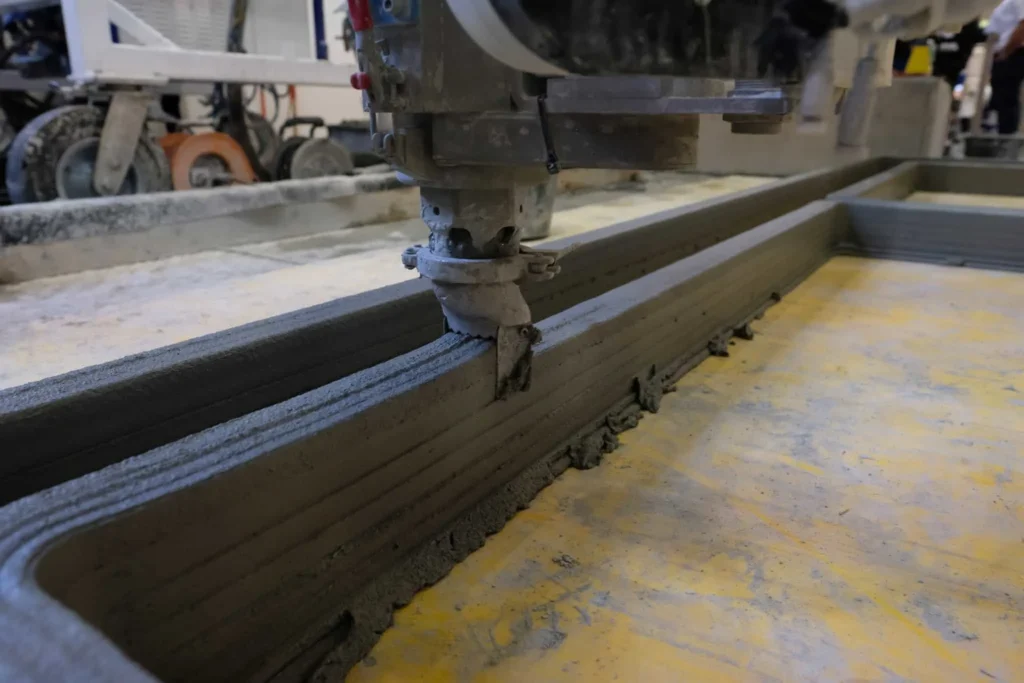 Close‑up of COBOD printer nozzle extruding a concrete layer on site