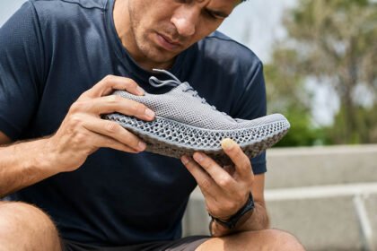 Person inspecting a 3D printed lattice shoe outdoors to check the TPU midsole for wear and durability.