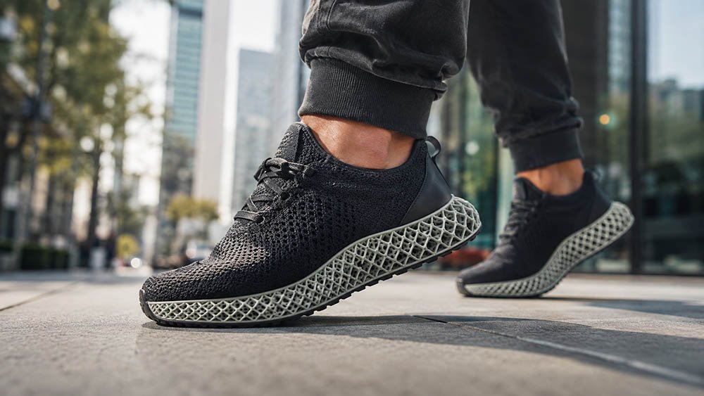 Person walking on an urban sidewalk wearing 3D printed lattice shoes with a visible TPU midsole structure.